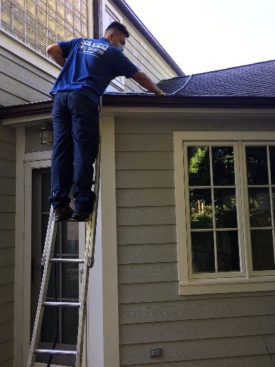 Technician on ladder cleaning a home's gutters.