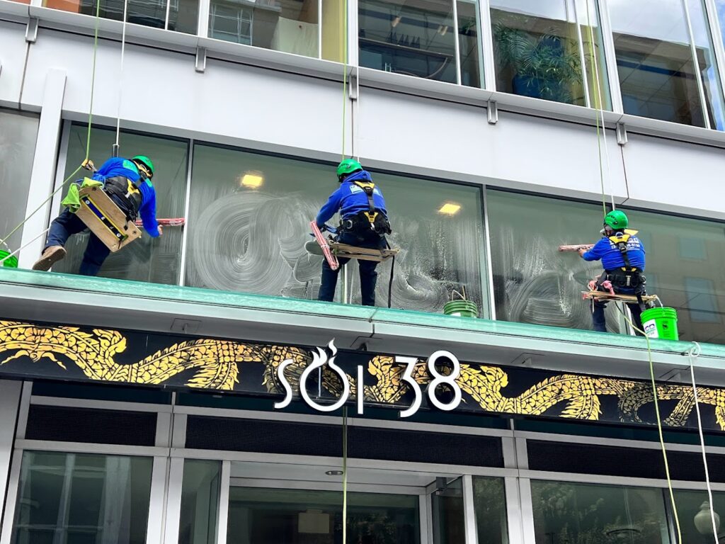 Window cleaners suspended by rope system, cleaning large windows on a commercial building.